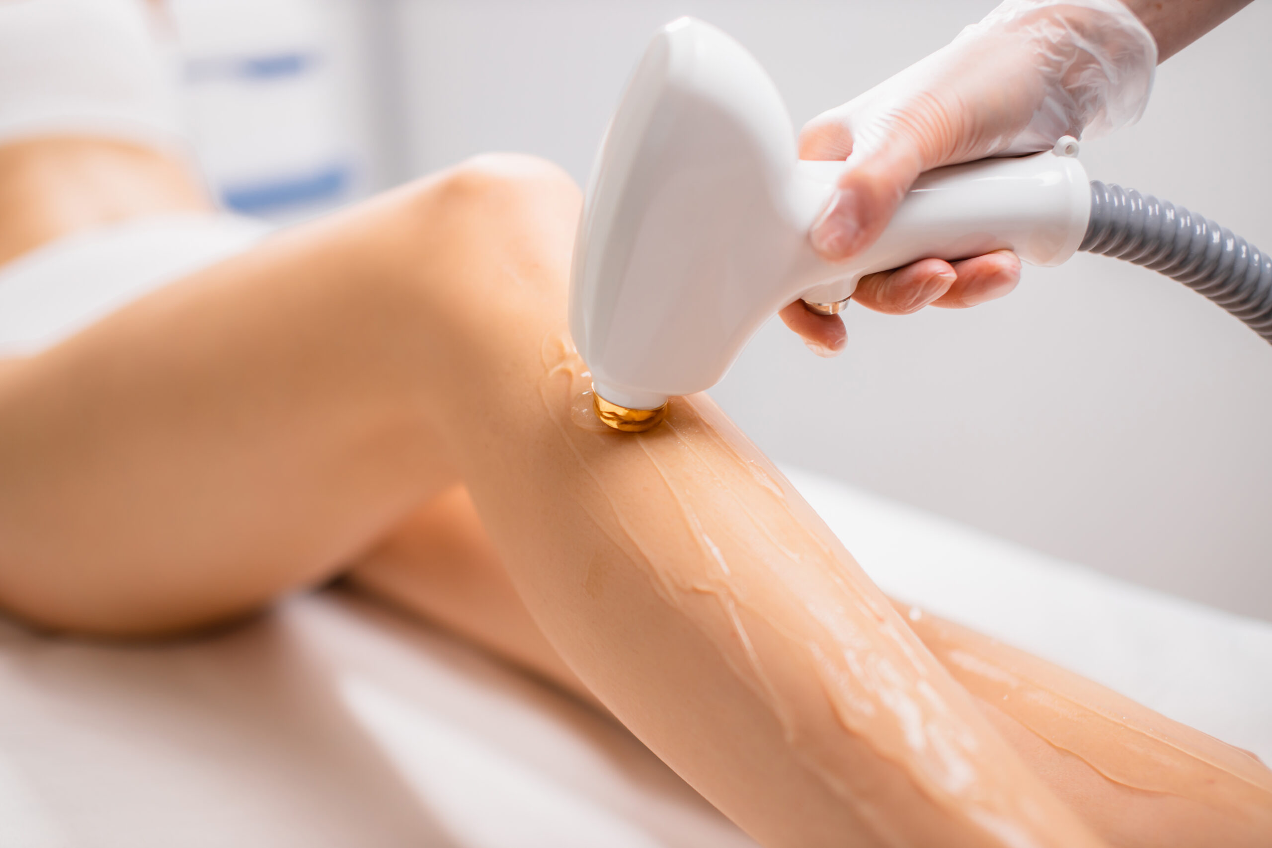 close-up woman's perfect legs while getting hair removal procedure in salon. professional beautician or cosmetologist use special ointment and apparatus. soft and smooth hairless skin on legs